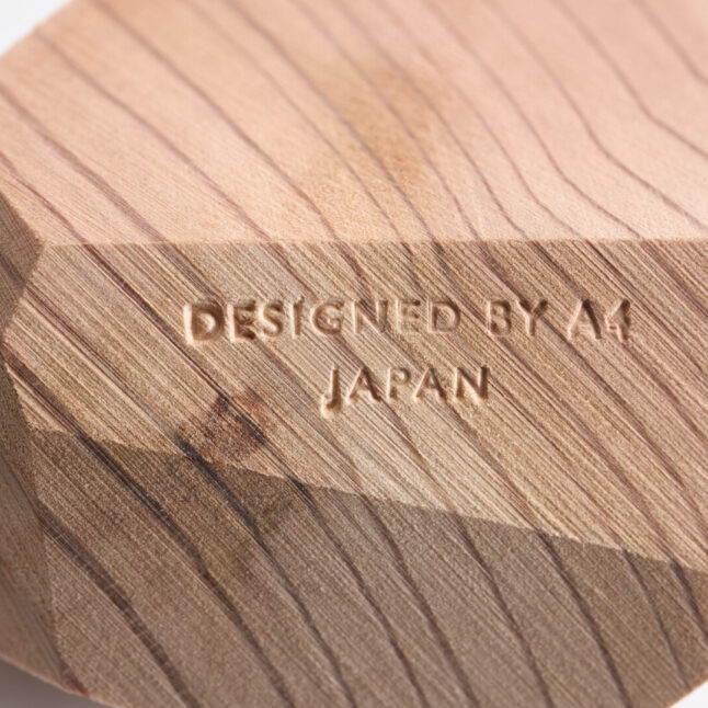 A close up of a natural red wood block with Designed by A4 Japan carved