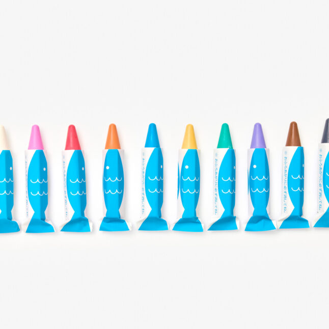 10 coloured crayons lined up next to each other. The crayons can be used on wet surfaces, therefore their wrapping features a bright blue and white illustration of a fish.