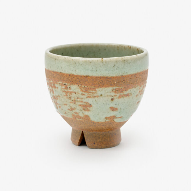 A rustic Japanese porcelain tea cup with a mix of mint blue and copper-red colours sitting on a white background
