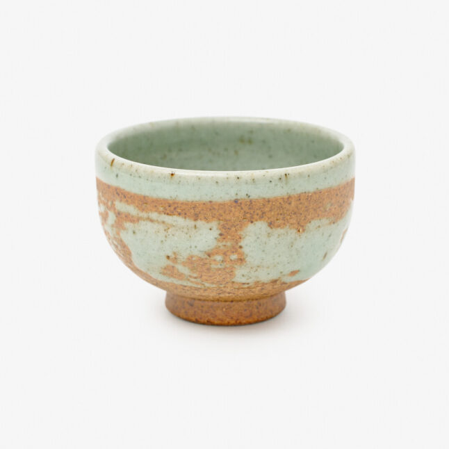 A Japanese porcelain sake cup with a mix of mint blue and copper-red colours sitting on a white background