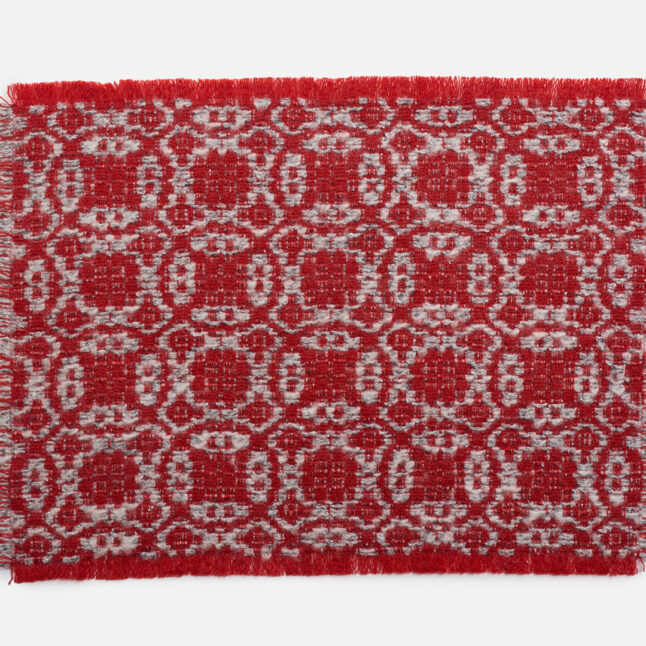 A wool table mat with a red background and grey pattern inspired by the snowflake on the flower from Japan House London.