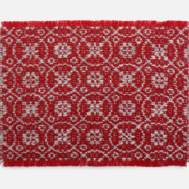 A wool table mat with a red background and grey pattern inspired by the snowflake on the flower from Japan House London.