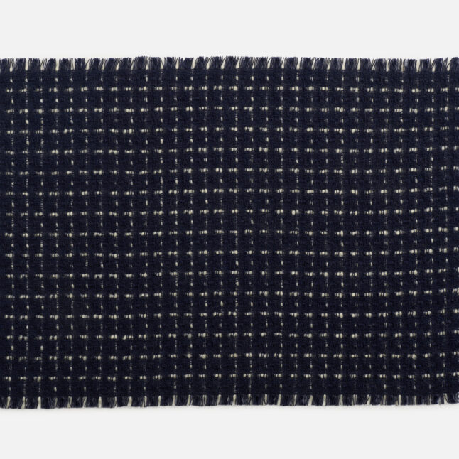 A wool table mat with a dark blue background and white check pattern from Japan House London.