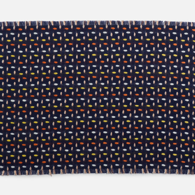 A wool table mat with a dark blue background and orange, yellow and white dots from Japan House London.