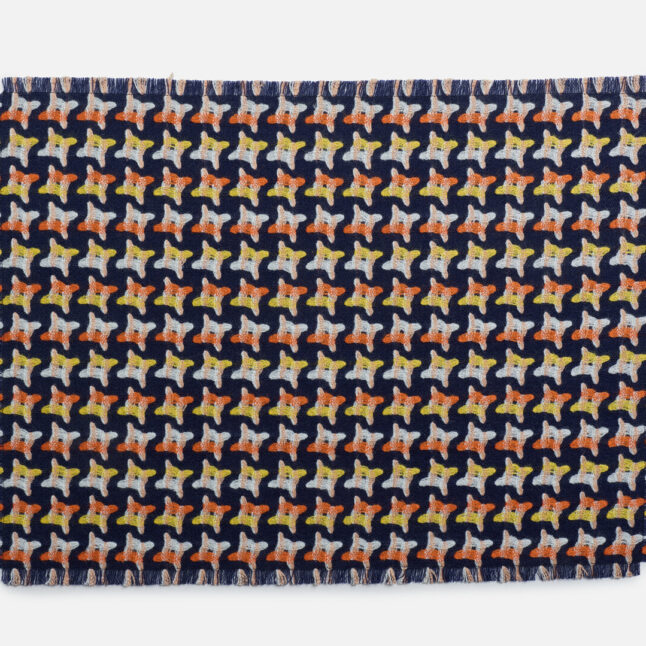 A wool table mat with a dark blue background and orange, yellow and white star-like shapes from Japan House London.
