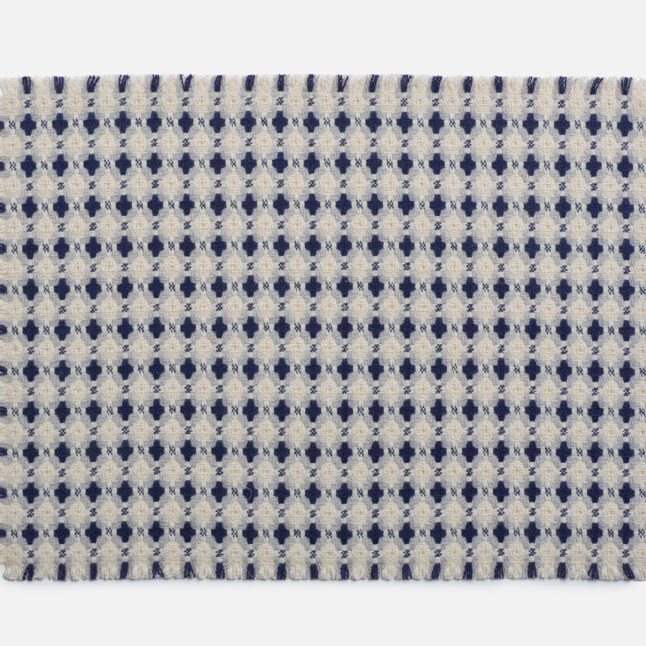 A wool table mat with a white background and blue check pattern from Japan House London.