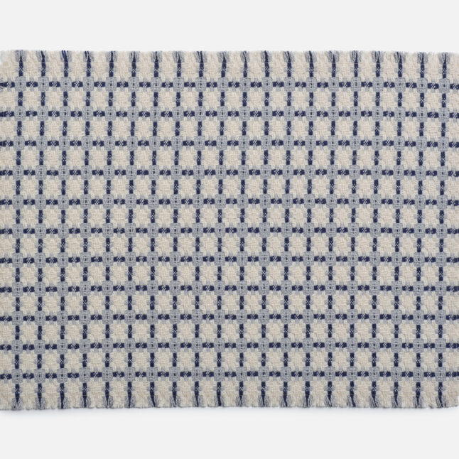 A wool table mat with a white background and blue check pattern from Japan House London.