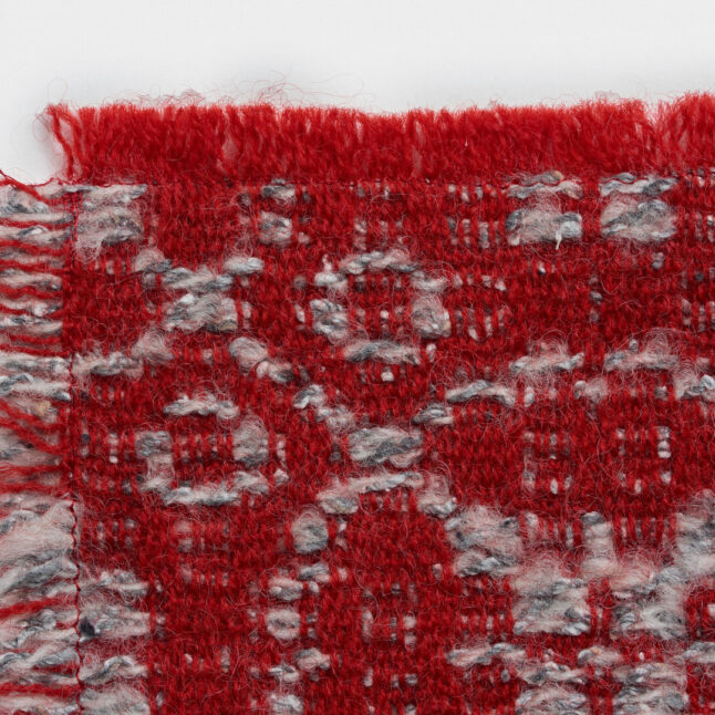 A wool table mat with a red background and grey pattern inspired by the snowflake on the flower from Japan House London.