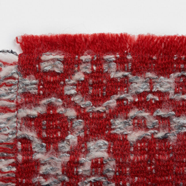 A wool table mat with a red background and grey pattern inspired by the snowflake on the flower from Japan House London.