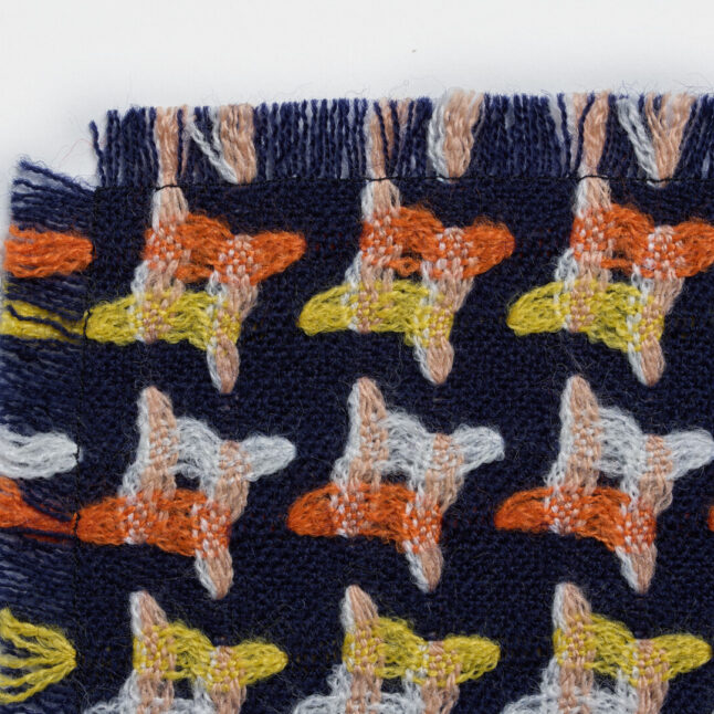 A wool table mat with a dark blue background and orange, yellow and white star-like shapes from Japan House London.