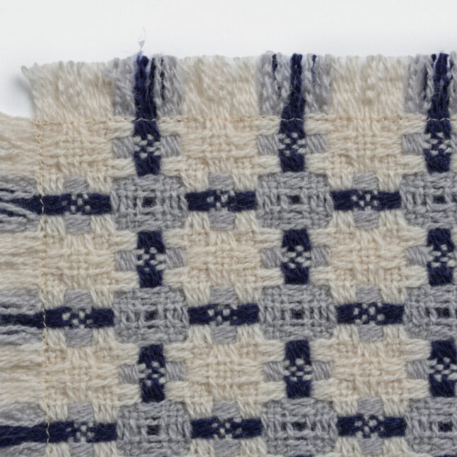 A wool table mat with a white background and blue check pattern from Japan House London.