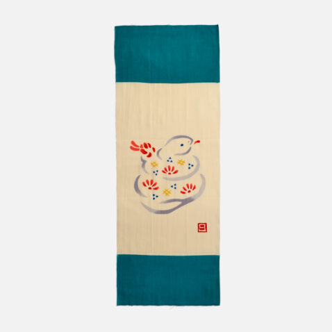 A cream cotton cloth with a illustration of a snake with markings of red, yellow and blue with a small square stamp of the makers from Japan House London.
