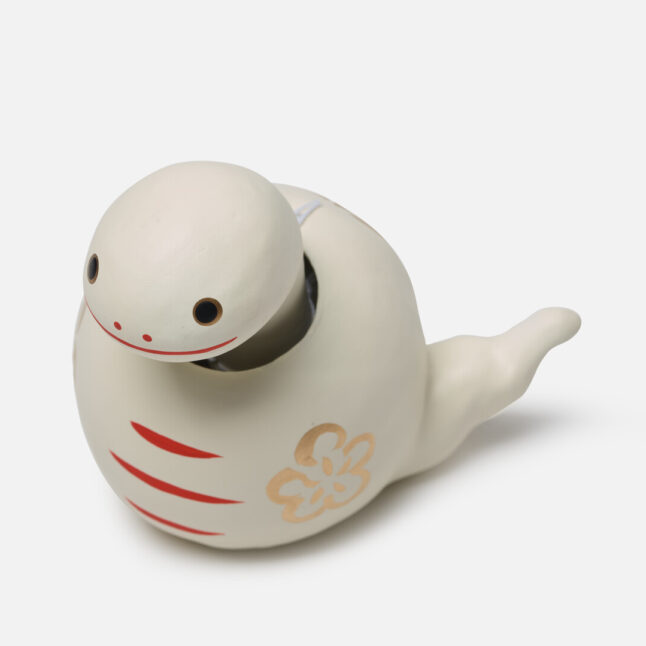 A figurine of a white paper snake with a bobbing head with gold and red markings from Japan House London.