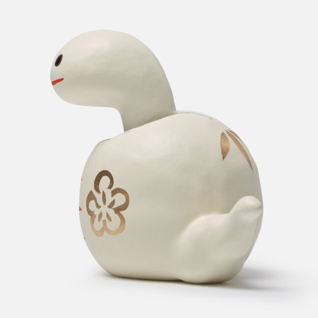 A figurine of a white paper snake with a bobbing head with gold and red markings from Japan House London.
