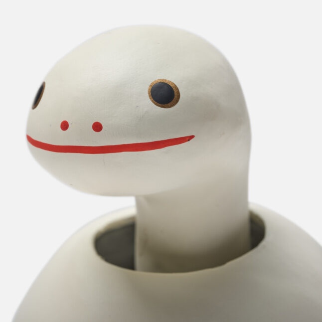 A figurine of a white paper snake with a bobbing head with gold and red markings from Japan House London.