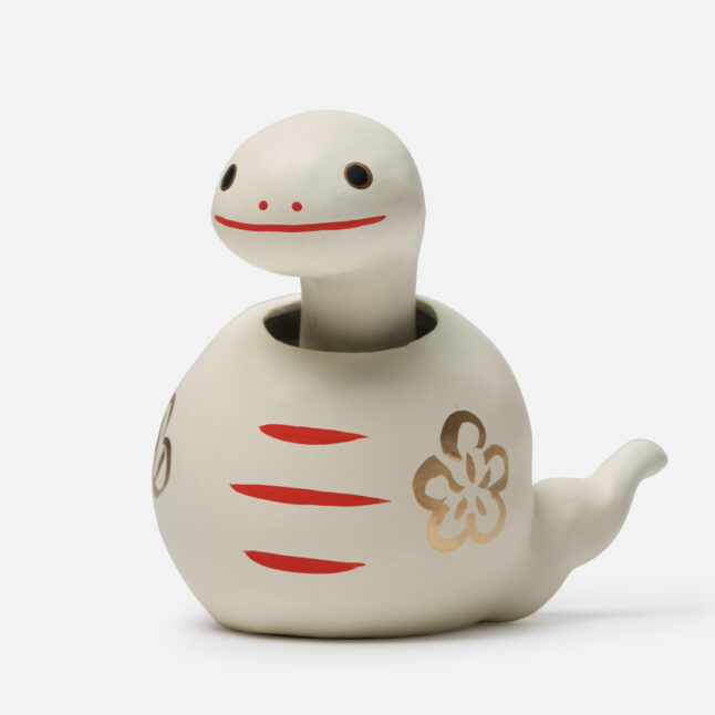 A figurine of a white paper snake with a bobbing head with gold and red markings from Japan House London.
