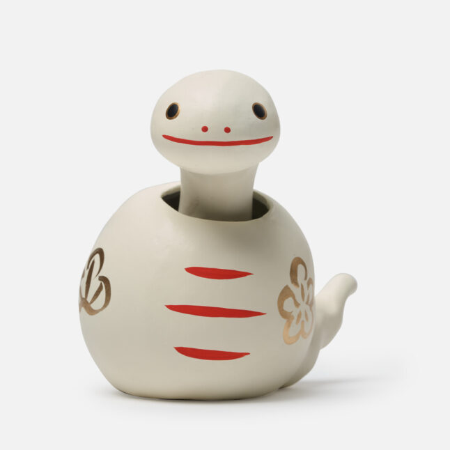 A figurine of a white paper snake with a bobbing head with gold and red markings from Japan House London.