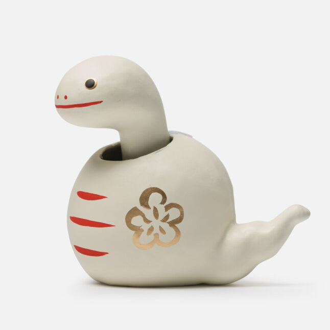 A figurine of a white paper snake with a bobbing head with gold and red markings from Japan House London.