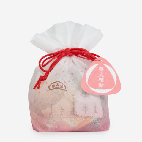 A drawstring bag with red string and a pink gradation holding sweets from Japan House London