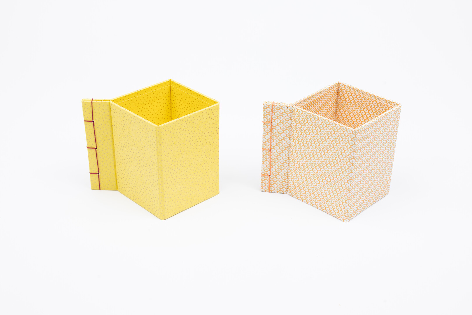 Two square paper pen pots, one yellow the other orange