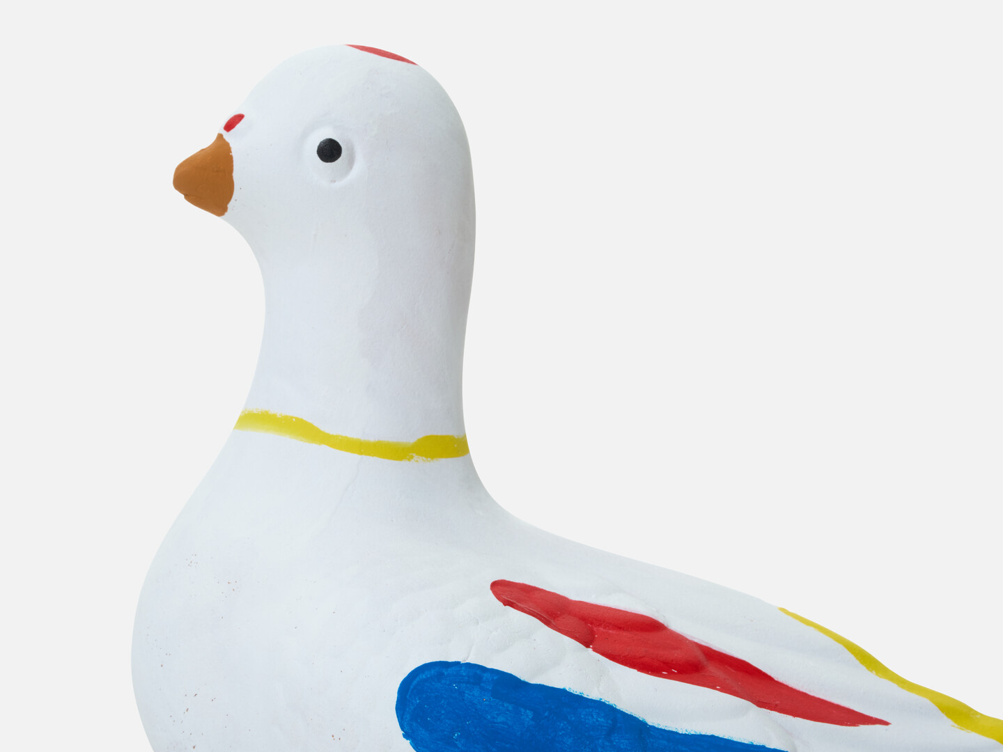 A head of a dove figurine with a yellow ring around the neck and yellow, red and blue markings from Japan House London.