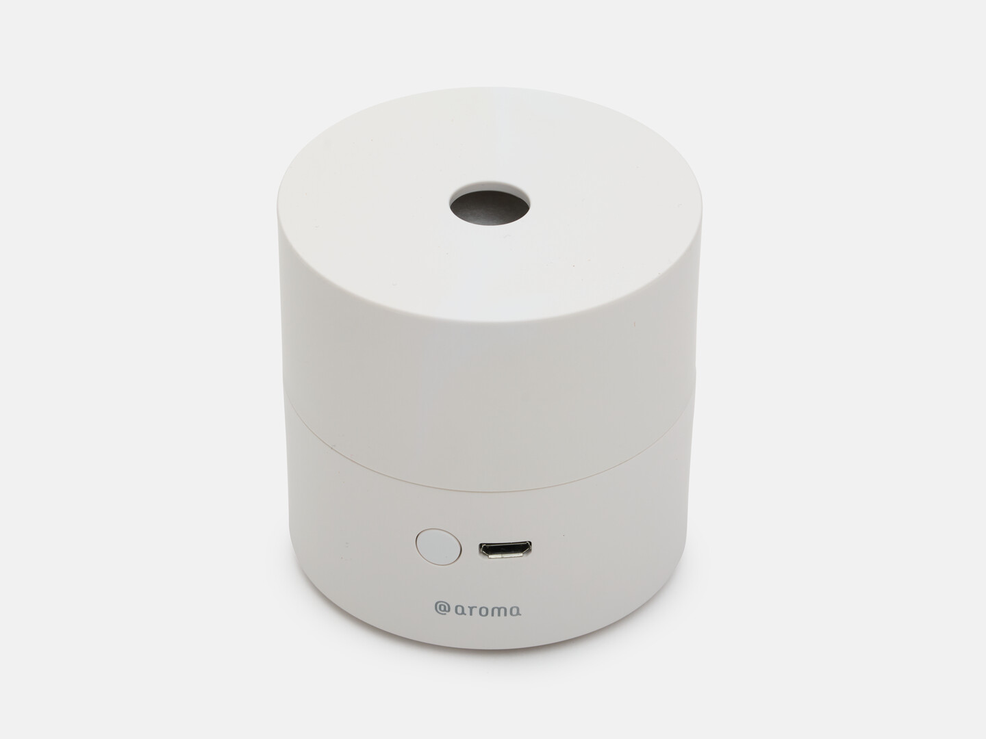 A white cylindrical minimal design aroma diffuser with a hole in the top for the aroma, a round button with a socket to plug in the USB cord