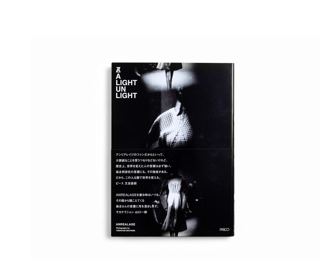 A black book with three photographs of bodies wearing outfits with the words A Light Un Light Anrealage Photography by Yoshiyuki Okuyama Parco