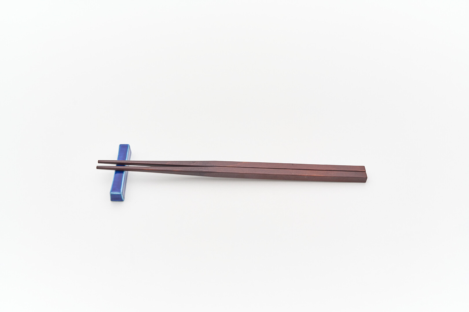 A dark wood chopstick with a blue porcelain chopstick rest