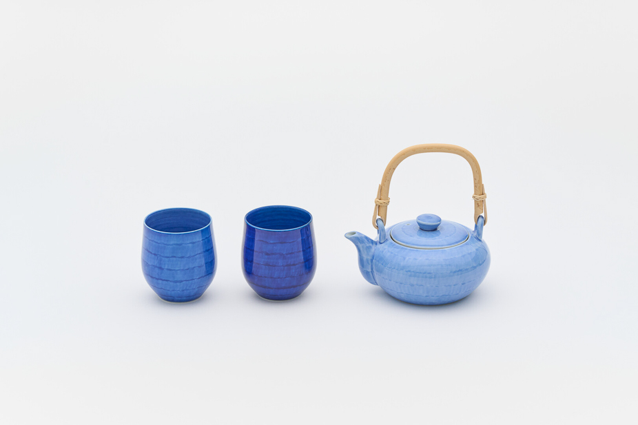 Two blue ceramic teacups and a blue ceramic kettle with bamboo handle