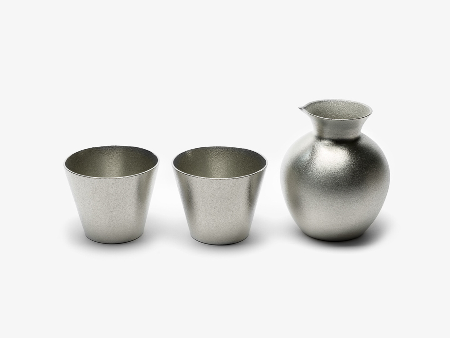 Two textured tin sake cups next to a tokkuri