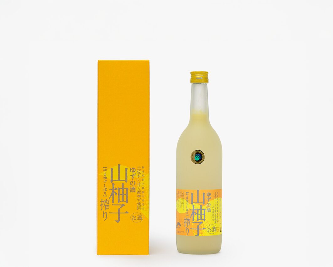 A yellow rectangular box with the words Tsukasabotan Yama Yuzu in Japanese next to a frosted glass bottle with a yellow liqueur and a yellow and orange label with the words Tsukasabotan Yama Yuzu