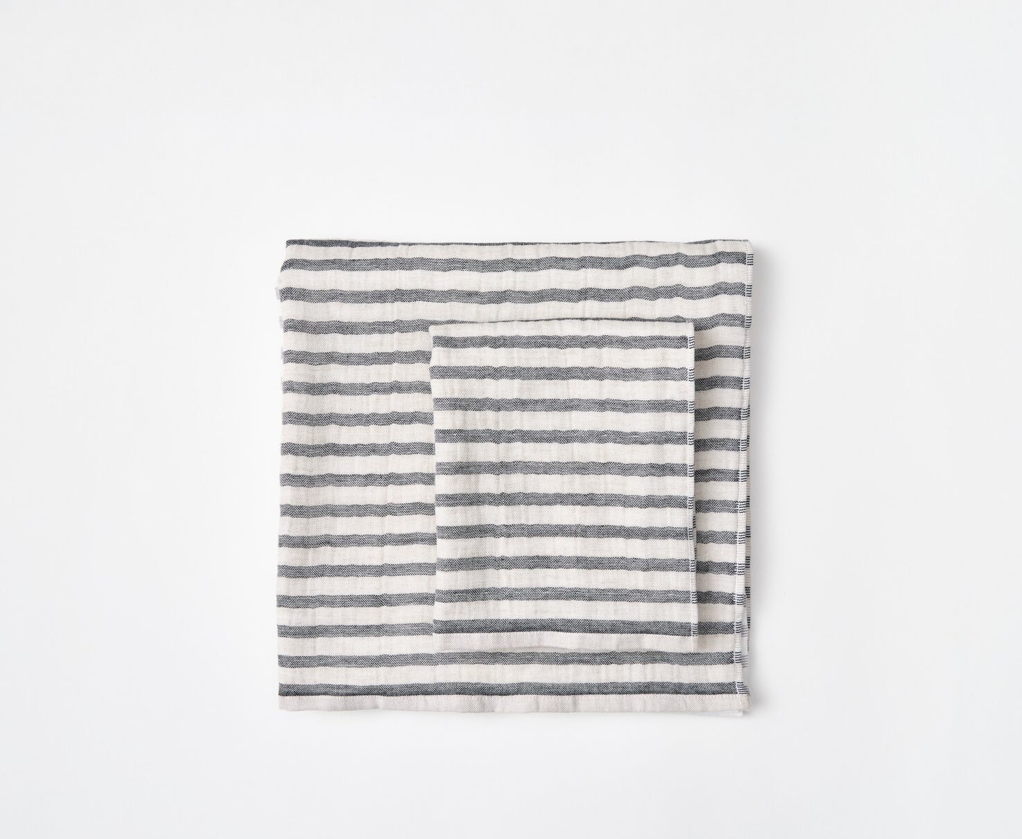 A large grey and white striped towel folded into a square with a smaller grey and white striped towel on top