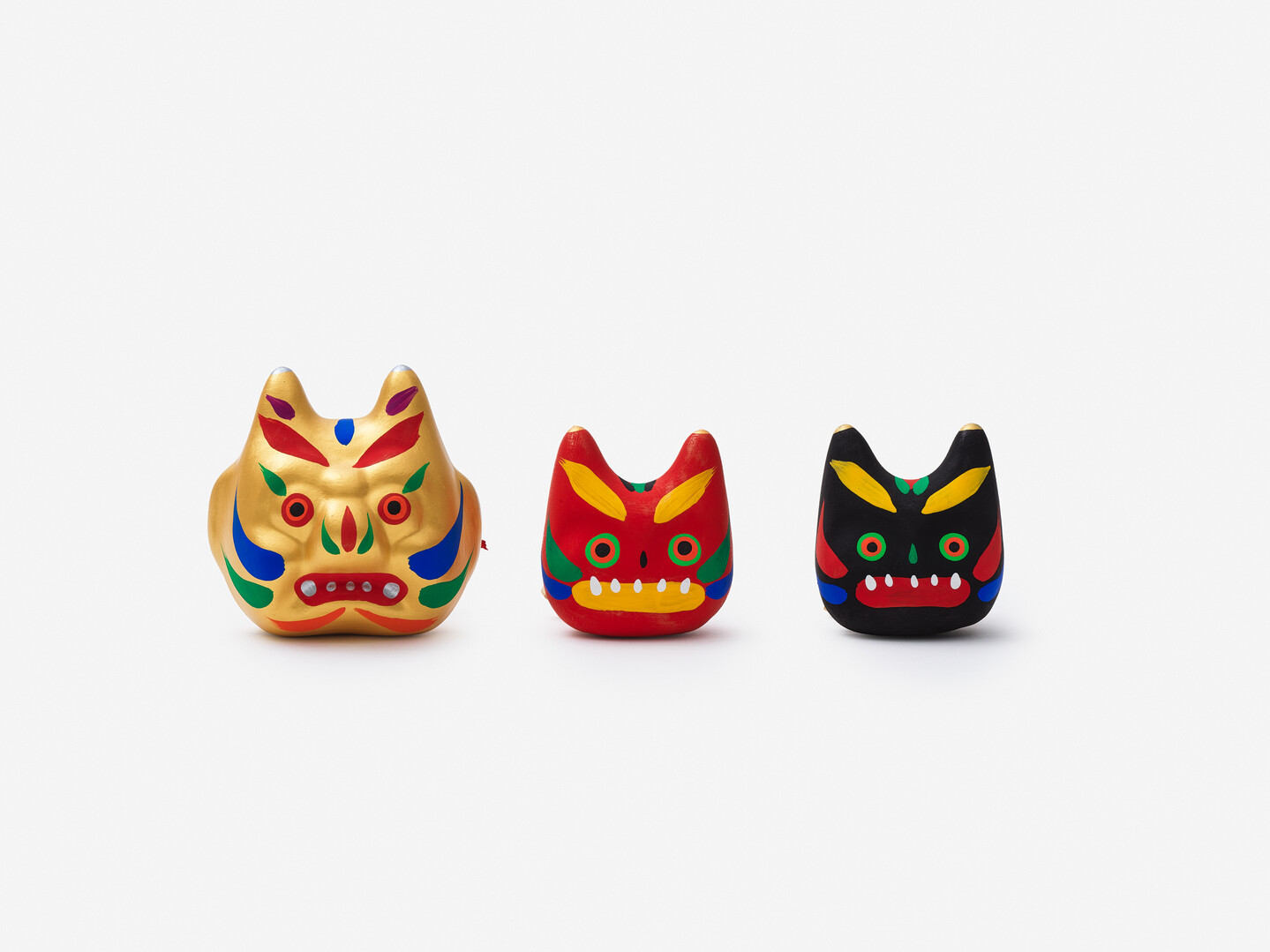 Three clay ogre heads in a row, one gold, one red and one black