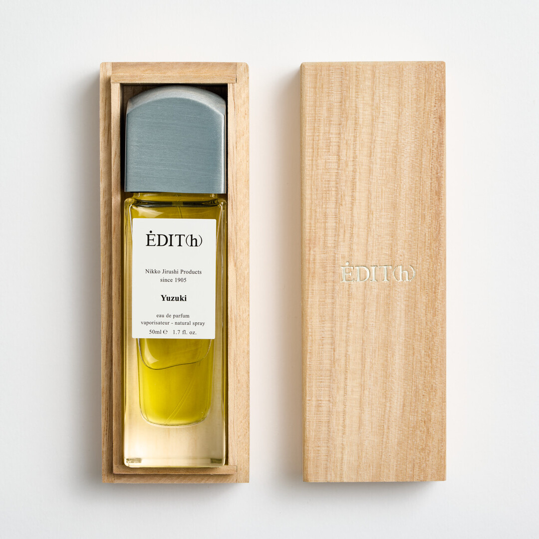 A tall rectangular perfume with a metal lid with EDIT(h) Nikko Jirushi Products since 1905 YUZUKI on the label in a wooden box