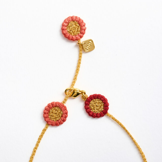 A textile necklace with gold chain connecting pink and red flowers
