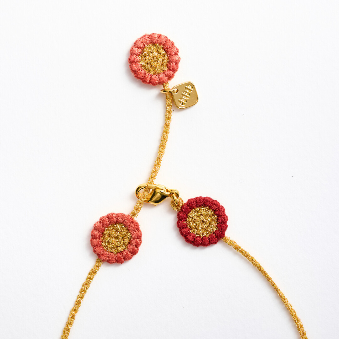 A textile necklace with gold chain connecting pink and red flowers
