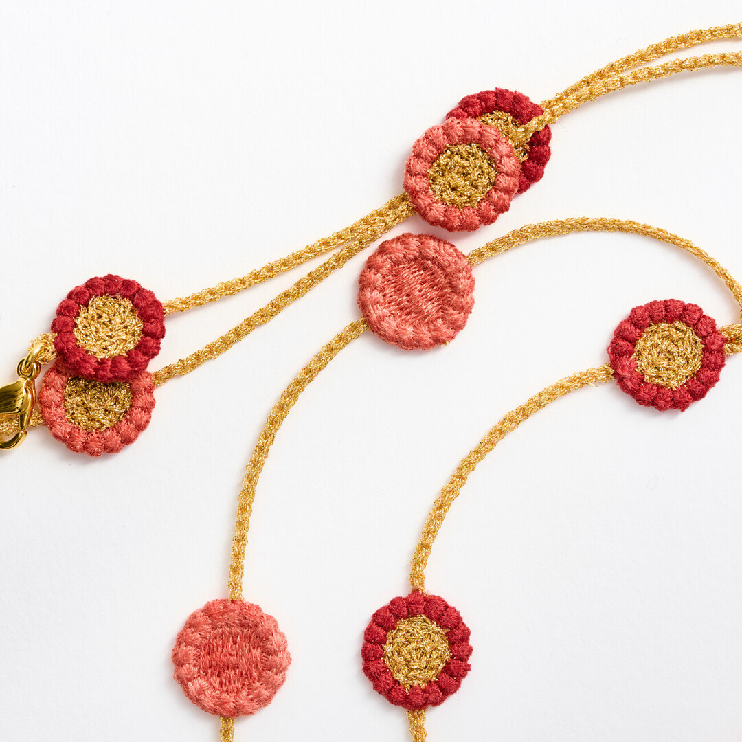 A textile necklace with gold chain connecting pink and red flowers