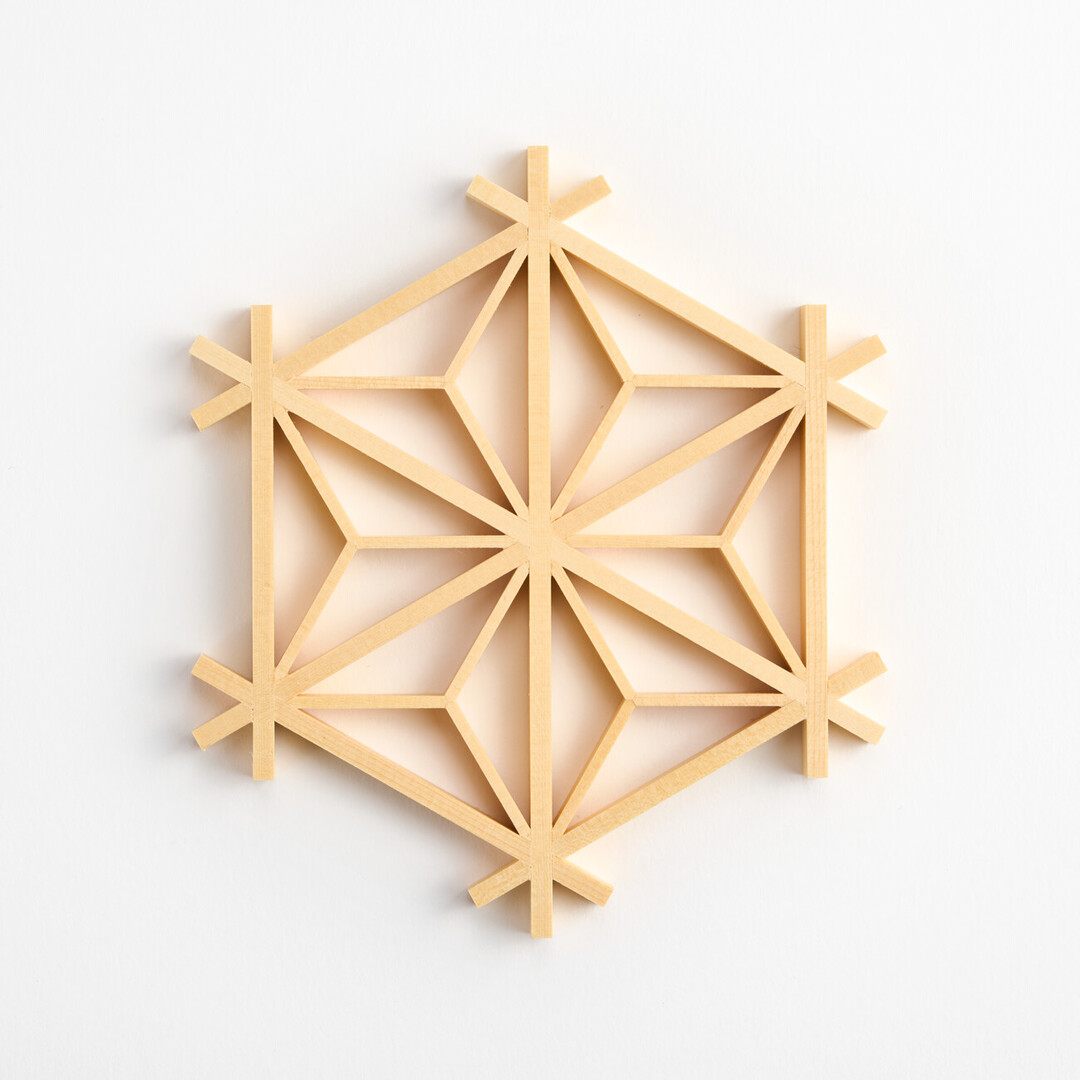 A wooden coaster made from strips of wood carefully assembled in a hemp leaf pattern