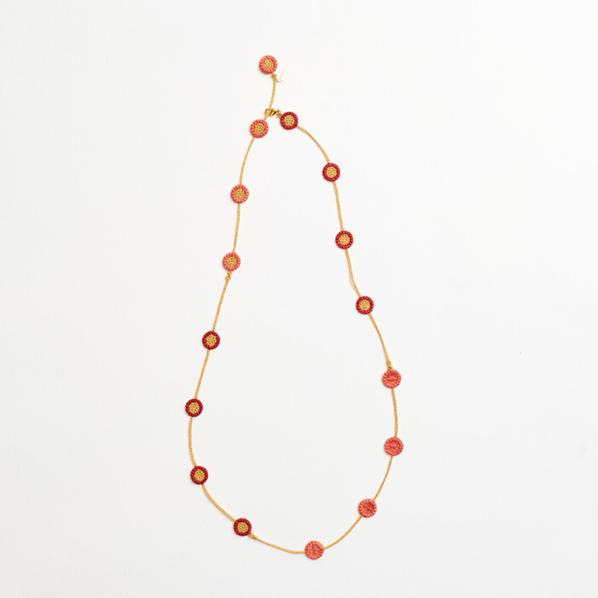A necklace with a gold textile chain and round orange and pink flowers evenly long the chain