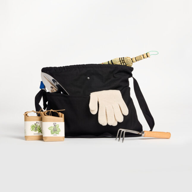 A black tote bag filled with gardening goods, of a hand shovel, gloves and a hand broom.