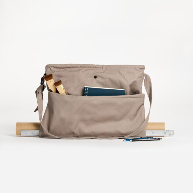 A grey tote bag with two brushes and a note book.