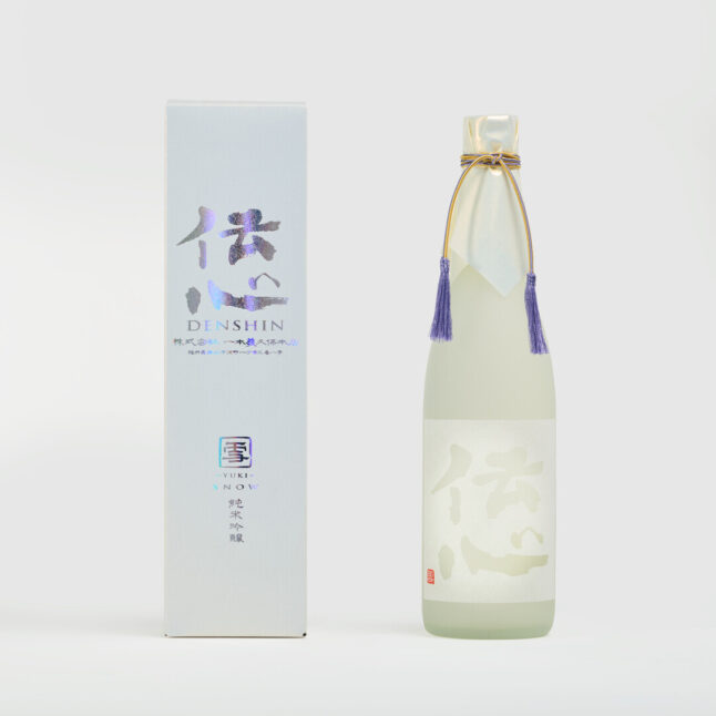 A white box with silver words of Denshin Junmai Ginjo sake next to a white bottle with a white label and a golden threads with purple tassles