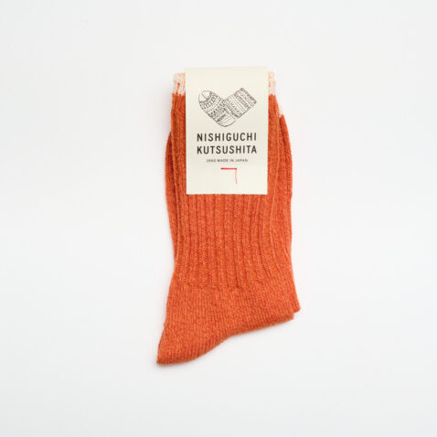 An orange sock with cream edge and white label with an illustration of a sock in black and the words Nishiguchi Kutsushita