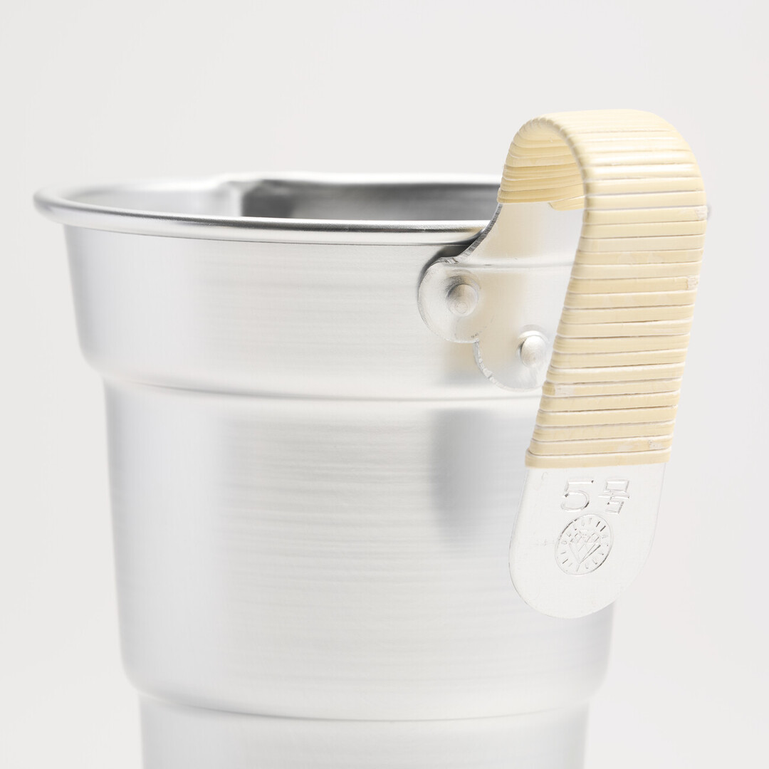 An aluminium sake pitcher with a bamboo wrapped handle. There is a detail of stamped at the end of the handle with the diamond mark of the brand and the words 5 gō