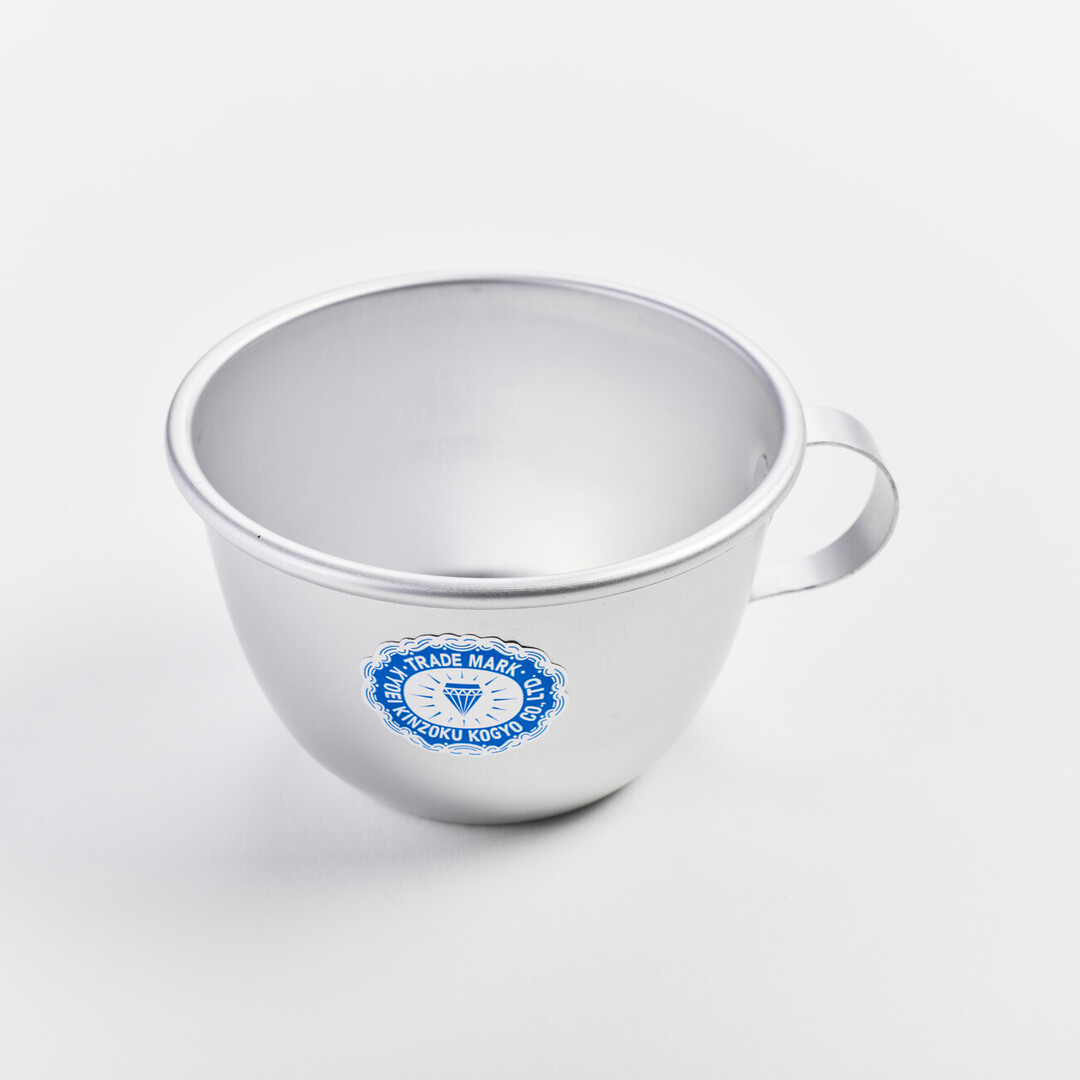 An small aluminium cup with a handle and sticker with a diamond and the words Tradmark Kyouei Kinzoku Kogyo Co., Ltd