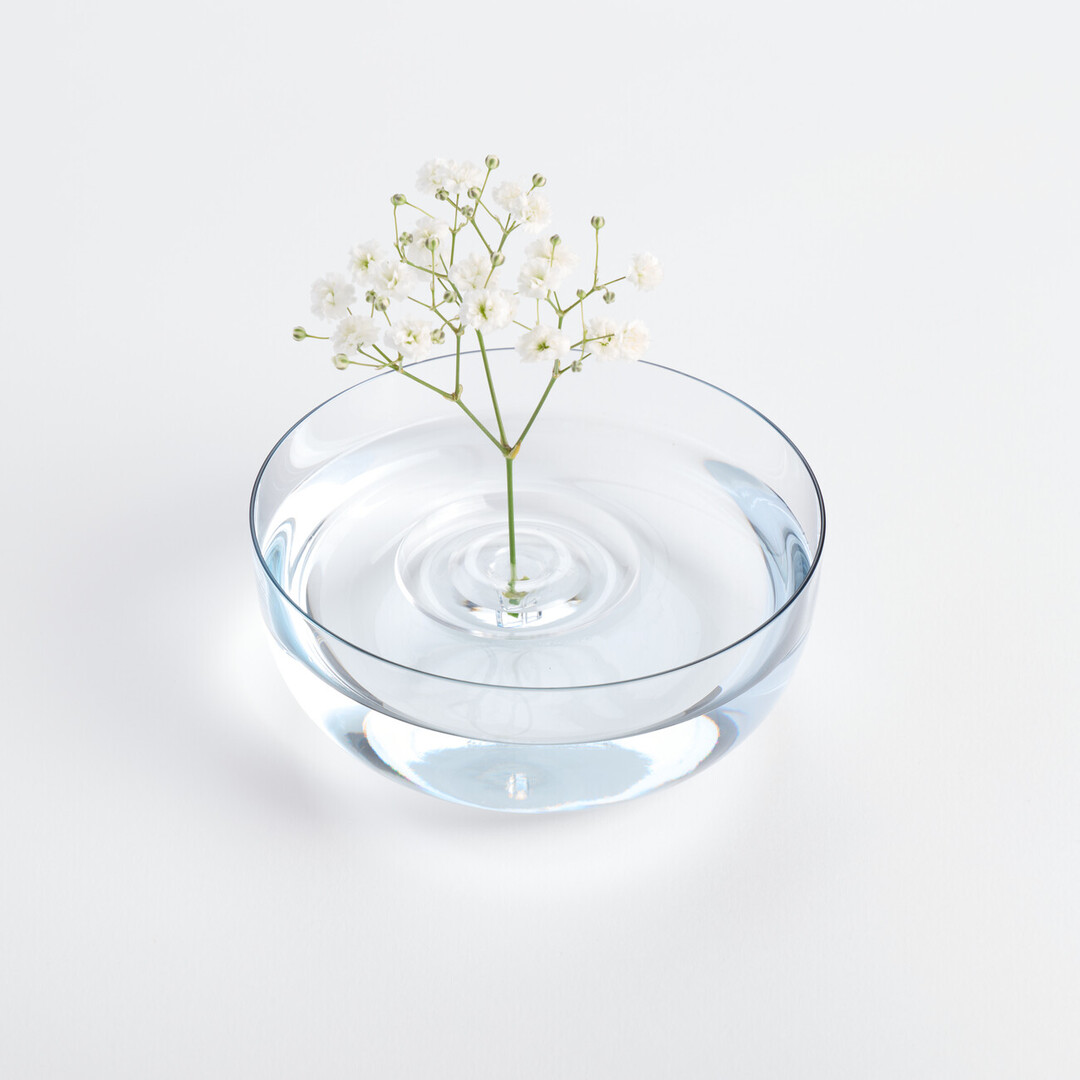 A bowl with a ripple shaped vase holding a stem of floating flowers