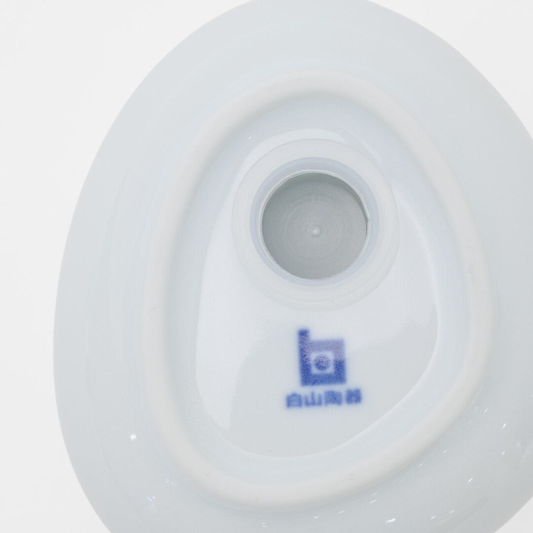 The underside of a white Hakusan Porcelain pepper shaker with the blue logo next to the hole to refill the pepper