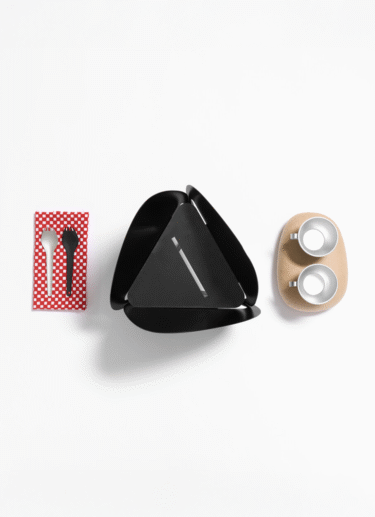 A collection of outdoor items such as two small aluminium cups on top of paper rock-shaped boxes, a laser-cut fire pit and two sporks on top of a red and white chequered tenugui.