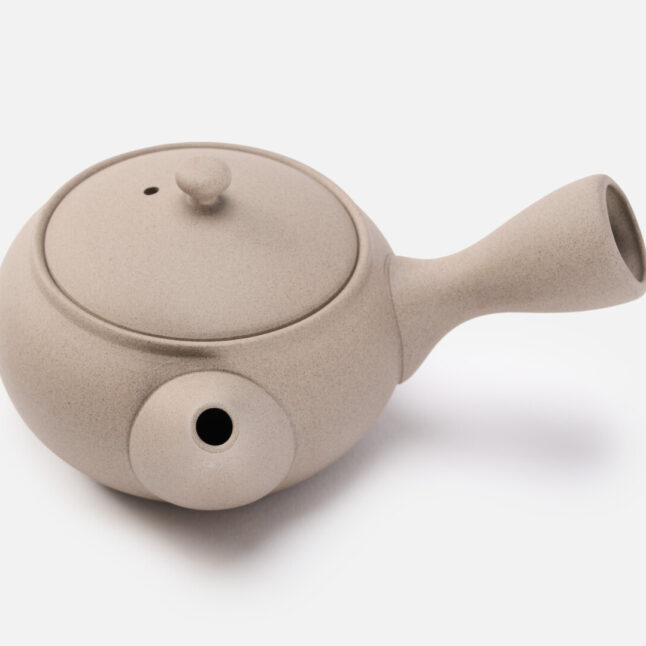 A beige rounded teapot for green tea with a handle on the side