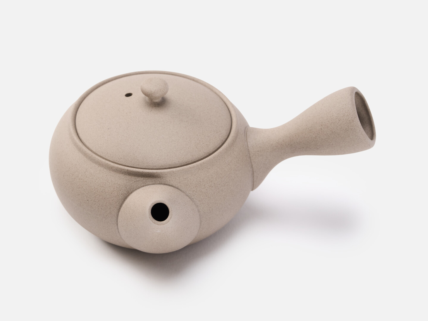 A beige rounded teapot for green tea with a handle on the side